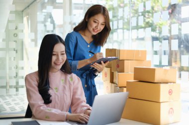 Asyalı küçük işletme sahibi ev ofisindeki arkadaşıyla birlikte çalışıyor. Ticari perakende pazarı ve çevrimiçi pazarlama dağıtımı, KOBİ e-ticaret kavramı