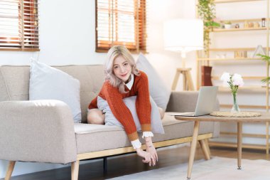 Güzel Asyalı kadın evde dinleniyor ve rahat bir kanepeye oturuyor..