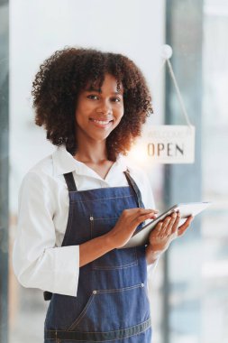 Güzel Amerikalı Afrikalı kafe sahibi kafede dikiliyor ve dijital tablet kullanıyor. Kafede, restoranda çalışmak..