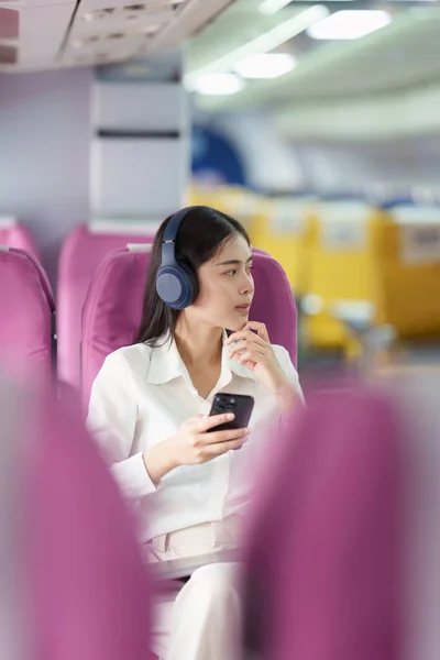 Piękna Azjatycka Bizneswoman Słuchać Muzyki Przez Telefon Komórkowy Podczas Lotu — Zdjęcie stockowe