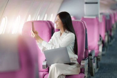 Güzel Asyalı iş kadını uçakla uçarken cep telefonuyla fotoğraf çekiyor. çalışma, seyahat, iş konsepti.