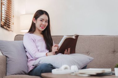 Çekici Asyalı kadın rahat bir oturma odasında dinleniyor ve kitap okuyor, rahatla, kanepe, yaşam tarzı..