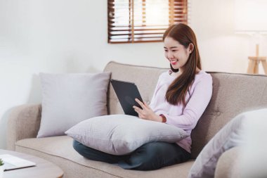 Çekici Asyalı kadın rahat oturma odasında dinleniyor ve dijital tablet kullanıyor, Rahat, Kanepe, Yaşam Tarzı.