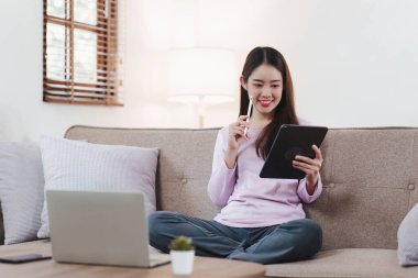 Çekici Asyalı kadın rahat oturma odasında dinleniyor ve dijital tablet kullanıyor, Rahat, Kanepe, Yaşam Tarzı.