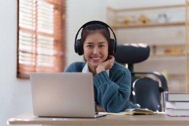 Çevrimiçi eğitim, e-öğrenme. Şık giyinmiş Asyalı bir kadın, dizüstü bilgisayar kullanıyor, online dersler dinliyor, notlar alıyor, evde online çalışmalar yapıyor..