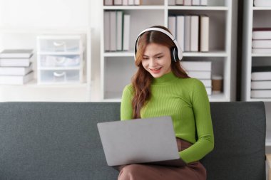 Çekici Asyalı kadın rahat oturma odasında dinleniyor ve dizüstü bilgisayar kullanıyor..