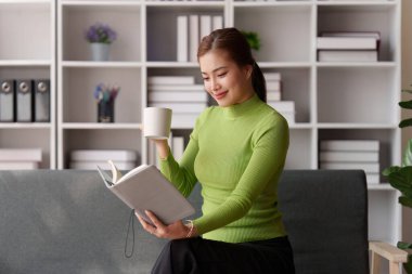 Çekici Asyalı kadın rahat bir oturma odasında dinleniyor ve kitap okuyor, rahatla, kanepe, yaşam tarzı..