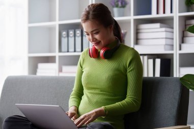 Çekici Asyalı kadın rahat oturma odasında dinleniyor ve dizüstü bilgisayar kullanıyor ve müzik dinliyor, rahatla, kanepe, yaşam tarzı.