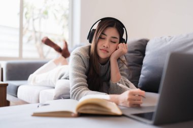 Çevrimiçi eğitim, e-öğrenme. Şık giyinmiş Asyalı bir kadın, dizüstü bilgisayar kullanıyor, online dersler dinliyor, notlar alıyor, evde online çalışmalar yapıyor..