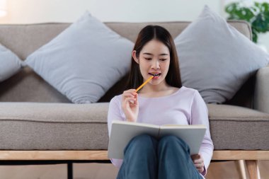 Çevrimiçi eğitim, e-öğrenme. Şık giyinmiş Asyalı bir kadın, dizüstü bilgisayar kullanıyor, online dersler dinliyor, notlar alıyor, evde online çalışmalar yapıyor..