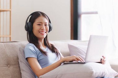 Çekici Asyalı kadın rahat oturma odasında dinleniyor ve dizüstü bilgisayar kullanıyor..