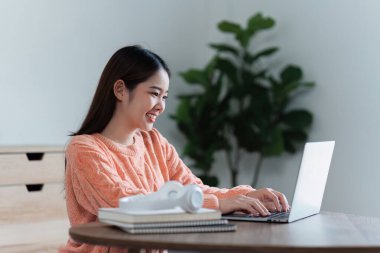 Çekici Asyalı kadın rahat oturma odasında dinleniyor ve dizüstü bilgisayar kullanıyor..