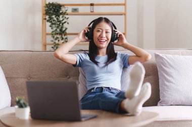 Çekici Asyalı kadın rahat oturma odasında dinleniyor ve dizüstü bilgisayar kullanıyor..