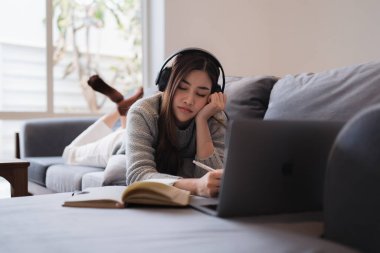 Çevrimiçi eğitim, e-öğrenme. Şık giyinmiş Asyalı bir kadın, dizüstü bilgisayar kullanıyor, online dersler dinliyor, notlar alıyor, evde online çalışmalar yapıyor..