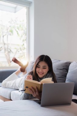 Çevrimiçi eğitim, e-öğrenme. Şık giyinmiş Asyalı bir kadın, dizüstü bilgisayar kullanıyor, online dersler dinliyor, notlar alıyor, evde online çalışmalar yapıyor..