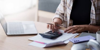 Asyalı muhasebe uzmanı ev faturalarını hesaplıyor, ev faturalarını inceliyor ve analiz ediyor ve vergi beyannamelerini dolduruyor...