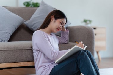 Çevrimiçi eğitim, e-öğrenme. Şık giyinmiş Asyalı bir kadın, dizüstü bilgisayar kullanıyor, online dersler dinliyor, notlar alıyor, evde online çalışmalar yapıyor..