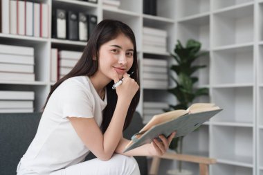 Çekici Asyalı kadın rahat bir oturma odasında dinleniyor ve kitap okuyor, rahatla, kanepe, yaşam tarzı..