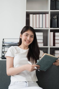 Çekici Asyalı kadın rahat bir oturma odasında dinleniyor ve kitap okuyor, rahatla, kanepe, yaşam tarzı..