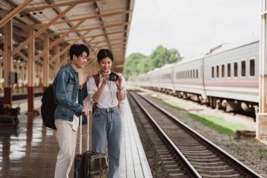 Tren istasyonundaki Asyalı çift çok mutlu. Turizm ve yaz seyahatleri.