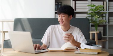 Çevrimiçi eğitim, e-öğrenme. Şık giyinmiş Asyalı bir adam, dizüstü bilgisayar kullanıyor, online dersler dinliyor, notlar alıyor, evde online çalışmalar yapıyor..