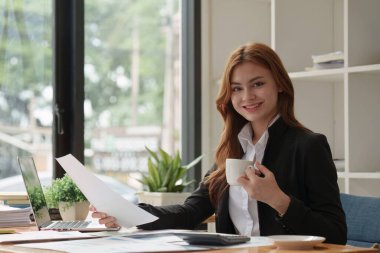 Dizüstü bilgisayarda çalışan ve belge, vergi, takas, araştırma, muhasebe ve mali danışman konsepti üzerinde çalışan muhasebeci kadın.