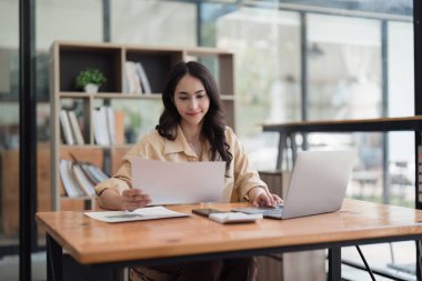 Dizüstü bilgisayarda çalışan ve belge, vergi, takas, araştırma, muhasebe ve mali danışman konsepti üzerinde çalışan muhasebeci kadın.