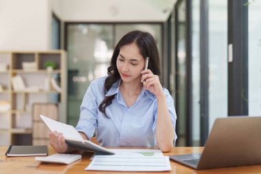 Asyalı bir kadın çalışıyor, dizüstü bilgisayar kullanıyor, finans şirketine rapor yazıyor. Muhasebe ve finansal kavram.