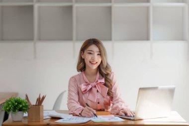 Gülümseyen Asyalı Muhasebeci mali raporu analiz eder ve yıllık rakamları inceler, karı analiz eder.