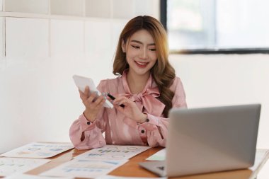 Gülümseyen Asyalı Muhasebeci mali raporu analiz eder ve yıllık rakamları inceler, karı analiz eder.