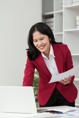 Gülümseyen Asyalı Muhasebeci mali raporu analiz eder ve yıllık rakamları inceler, karı analiz eder.