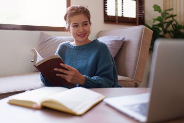 Asyalı bir kadın rahat bir koltukta oturup kitap okuyor..