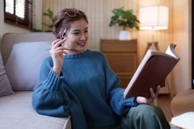 Asyalı bir kadın rahat bir koltukta oturup kitap okuyor..