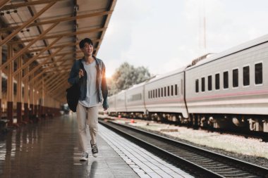 Asyalı turist, tren istasyonuna gitmek için sırt çantasıyla seyahat ediyor. Turizm ve yaz seyahatleri.