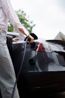 Elektrikli araba şarj oluyor, kadın arabaya elektrik kablosu bağlıyor. Yeşil Enerji kavramı.