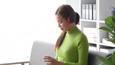 Çekici Asyalı kadın rahat oturma odasında dinleniyor ve dizüstü bilgisayar kullanıyor ve müzik dinliyor, Rahat, Kanepe, Yaşam Tarzı. Yüksek kalite 4k görüntü