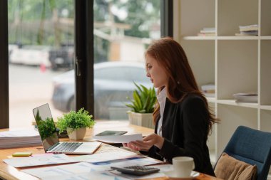 Dizüstü bilgisayarda çalışan ve belge, vergi, takas, araştırma, muhasebe ve mali danışman konsepti üzerinde çalışan muhasebeci kadın.