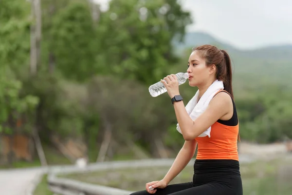 Woman drinking water after sport activities. Female exercising at outdoor park.