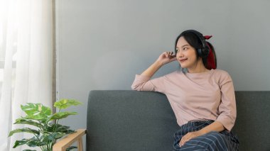 Genç bayan kanepede oturup müzik dinliyor, rahatlıyor ve gülümsüyor..