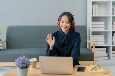 Asyalı genç bir kadın oturma odasındaki dizüstü bilgisayardan selam söylüyor. Kulaklık takan genç bir kadın evdeki bir laptopta görüşme yapıyor. Öğrenci çevrimiçi çalışırken notlar alıyor.