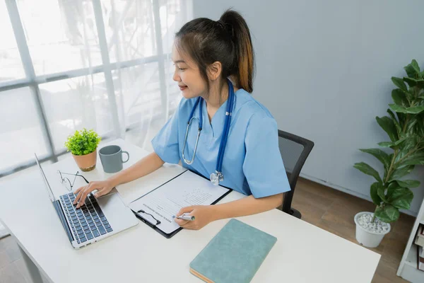 Profesyonel Asyalı kadın doktor klinikte masa başında çalışırken dizüstü bilgisayar kullanıyor..