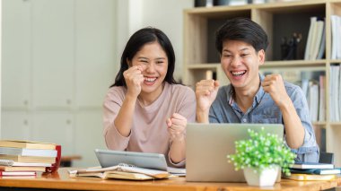 İki Asyalı öğrenci birlikte öğreniyor ve kafe 'de birlikte ders veriyor ve sınav sonuçlarını izlerken kutlama yapıyorlar..