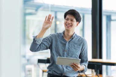 Genç işadamı arkadaşlarıyla selamlaşırken dijital tabletle çevrimiçi çalışıyor.