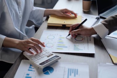 İş adamlarından oluşan ekip çalışması ofiste evrak işlerini finanse etmek için hesap makinesini tartışır ve kullanır.