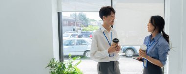 İki genç Asyalı iş kadını ofiste sohbet ediyor ve kahve içiyorlar..