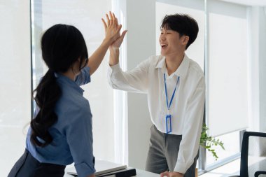 Mutlu Asyalı erkek ofis çalışanı projenin başarısını kutlamak için bayan meslektaşına beşlik çakıyor..