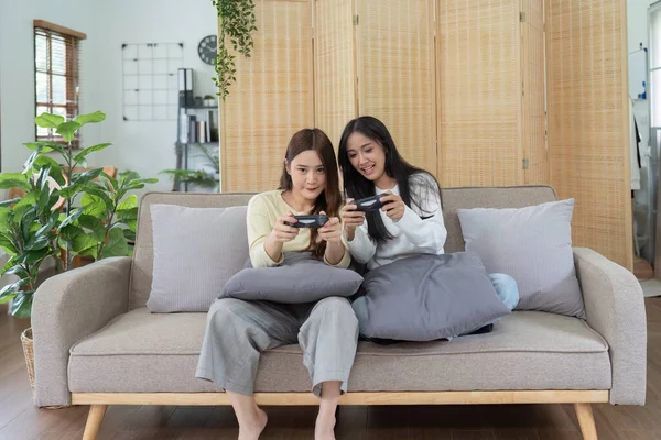 Asian beautiful lesbian gay couple enjoy play game together in Livingroom. Two female friend sit on sofa in living room, feel happy to play joystick game at home..