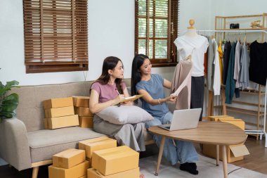 İş yerinde bilgisayarla çalışan küçük bir işletme sahibi. Serbest çalışan iki kadın satıcı ürün siparişini kontrol ediyor. Müşteriye teslimat için mal paketliyorum. Çevrimiçi satış. E-ticaret. Nakliye kavramı.
