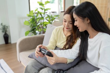 Asyalı güzel lezbiyen eşcinsel çift Livingroom 'da birlikte oyun oynuyorlar. İki bayan arkadaş oturma odasında kanepede oturur, evde joystick oynamaktan mutlu olurlar...