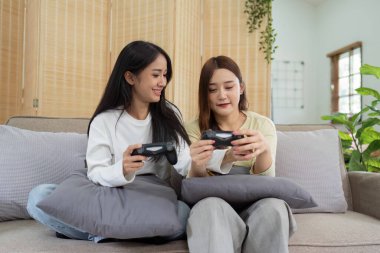 Asyalı güzel lezbiyen eşcinsel çift Livingroom 'da birlikte oyun oynuyorlar. İki bayan arkadaş oturma odasında kanepede oturur, evde joystick oynamaktan mutlu olurlar...